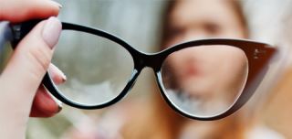 Person holding glasses with blurred lenses representing vision problems from dry eyes