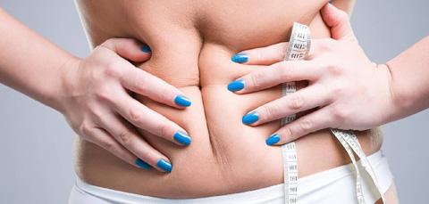 Patient holding abdominal skin with measuring tape illustrating concerns after bad liposuction and need for revision treatment