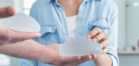 Patient holding silicone breast implants during consultation about breast implant replacement surgery
