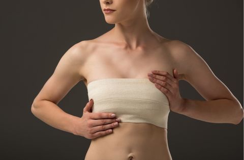 Woman with post-mastectomy bandage gently holding chest after breast reconstruction surgery