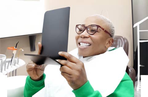 Smiling dental patient holding a mirror to admire newly treated teeth during post-procedure check-up