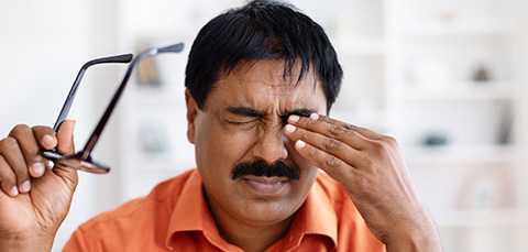 Man rubbing eyes in discomfort after removing glasses, showing link between dry eyes, headaches, and migraine pain.