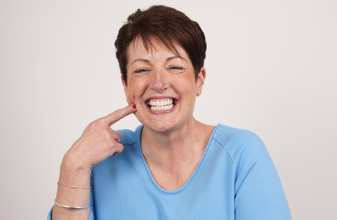 Female patient smiling and pointing at teeth after successful smile design treatment