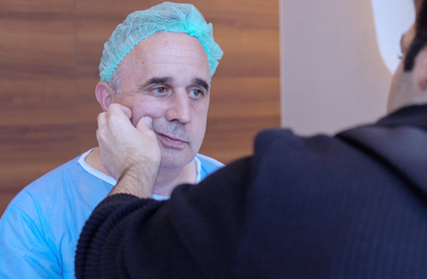 Surgeon examining male patients cheek during pre-op consult for buccal fat removal