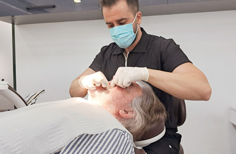 Dentist performing dental treatment on senior male patient in clinic chair