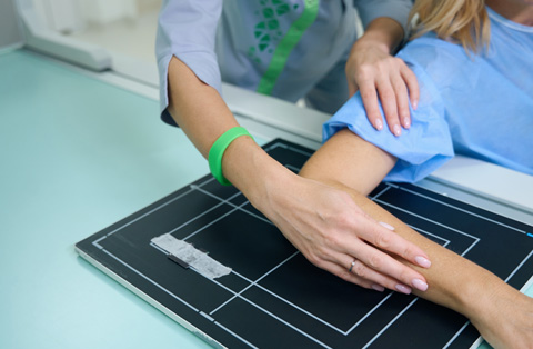 Medical professional positioning womans arm for X-ray to assess upper extremity injury
