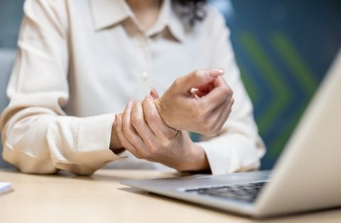 Woman holding her wrist in pain while working on laptop, showing carpal tunnel symptoms